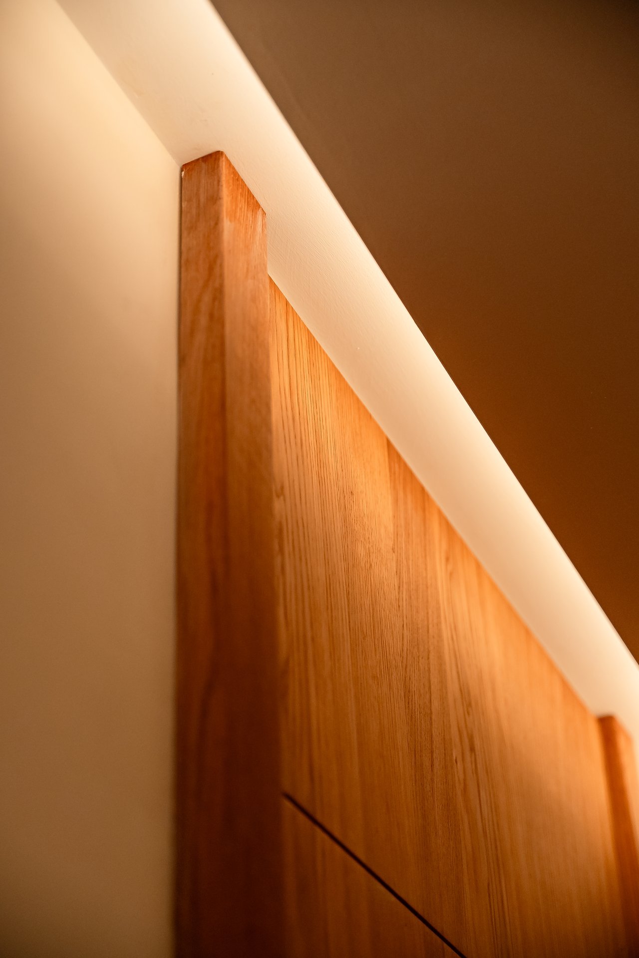 Panel de madera clara con veta natural, iluminado por tira LED cálida en el borde superior.